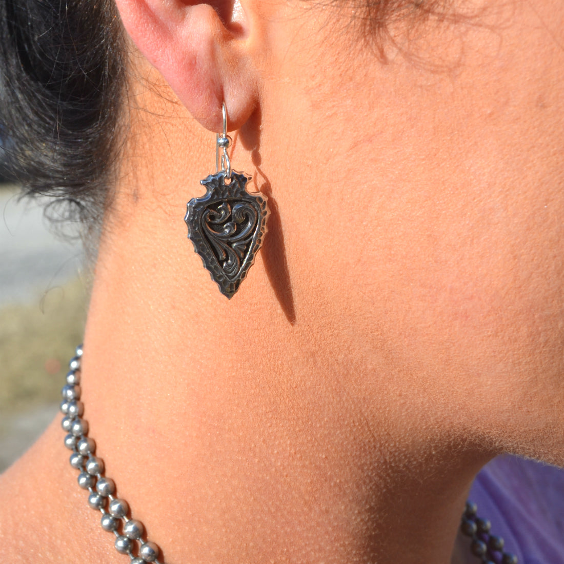 solid sterling silver dangle earrings with a delicate western style engraved scrolling inlaid in the middle of the piece. They measure at 1" long by 3/4" wide.