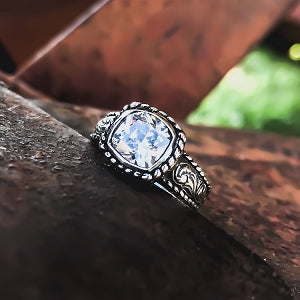 The "Lil Victoria" is a handmade sterling silver ring that has a unique rope border around the 8mm cushion cut cubic zirconia in a bezel setting as well as on either side of this beautiful ring. The unique rope border surrounds the western style hand engraving on either side of its band giving this ring the perfect touch of western elegance.