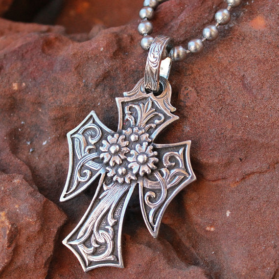 The "CoCo Cross" Necklace is a custom solid sterling silver cross pendant with an overlaid western style scroll hand engraving and features a very detailed cluster of four flowers overlaid in the center of the cross. This cross measures at 1 1/2" X 2 1/4".