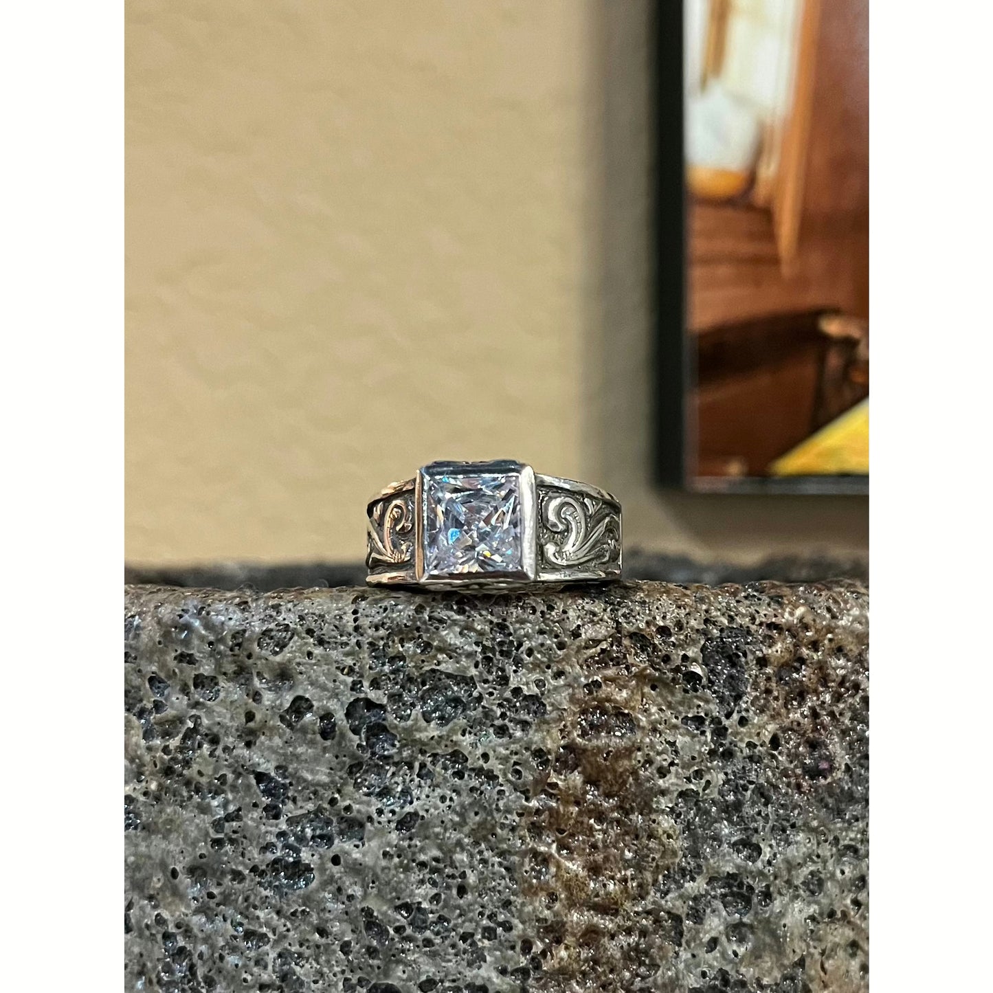 "Farrah" is a solid sterling silver custom ring with a low-profile bezel set 8 mm princess cut cubic zirconia. This beautiful unique ring features hand engraved scrolls on each side of the band with intricate scroll work on the front and back edges of the ring including around the stone. This elegant rings tapered band offers our most comfortable fit.