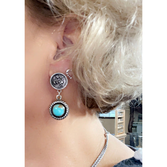 Sterling silver bucking bronc post earrings with an 8mm Kingman turquoise drop compliment by a roped border and an antique finish.