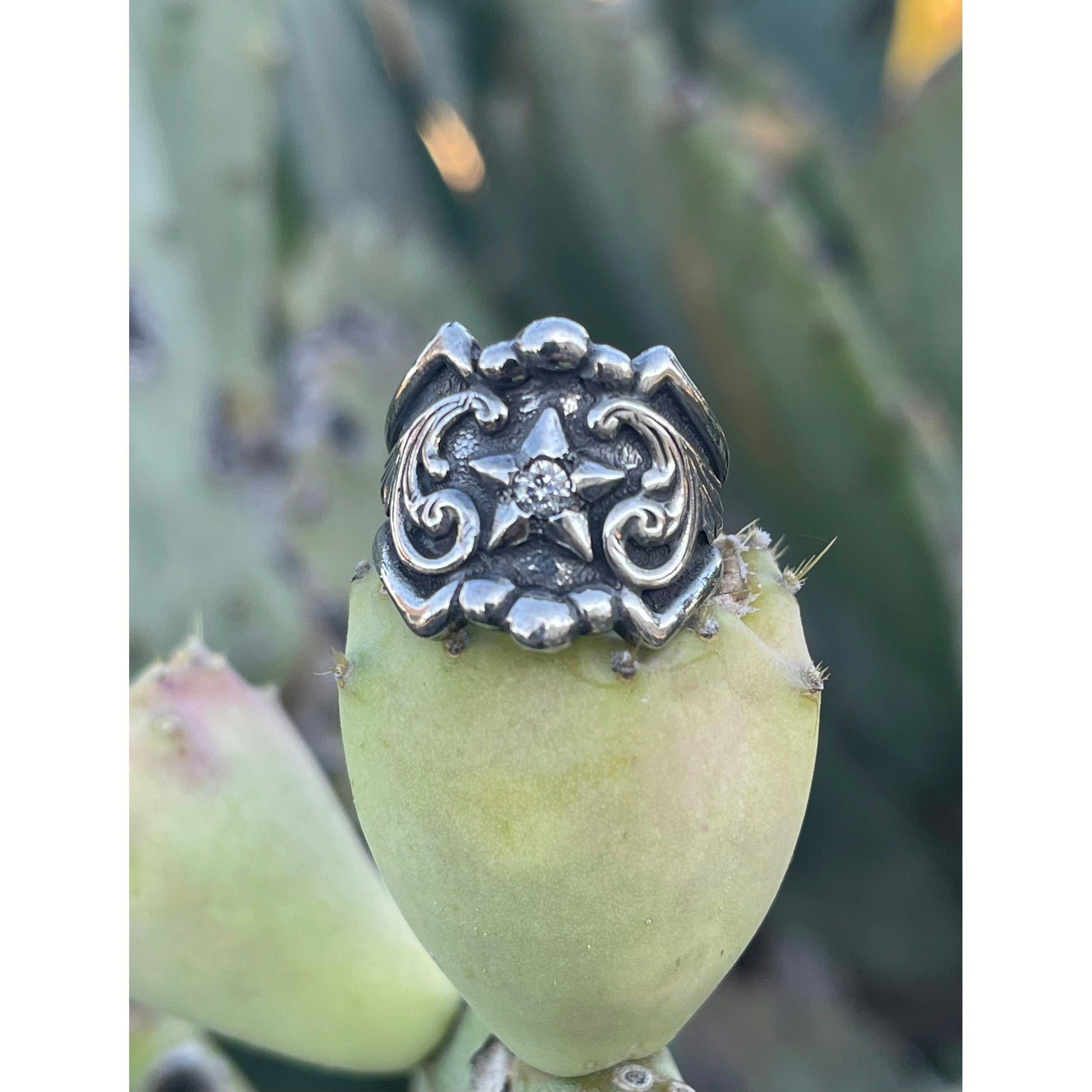 "Texas Star" is a solid sterling silver ring that has a unique border featuring an overlaid star in the setting and overlaid western style engraved scrolling on either side of the tapered band.
