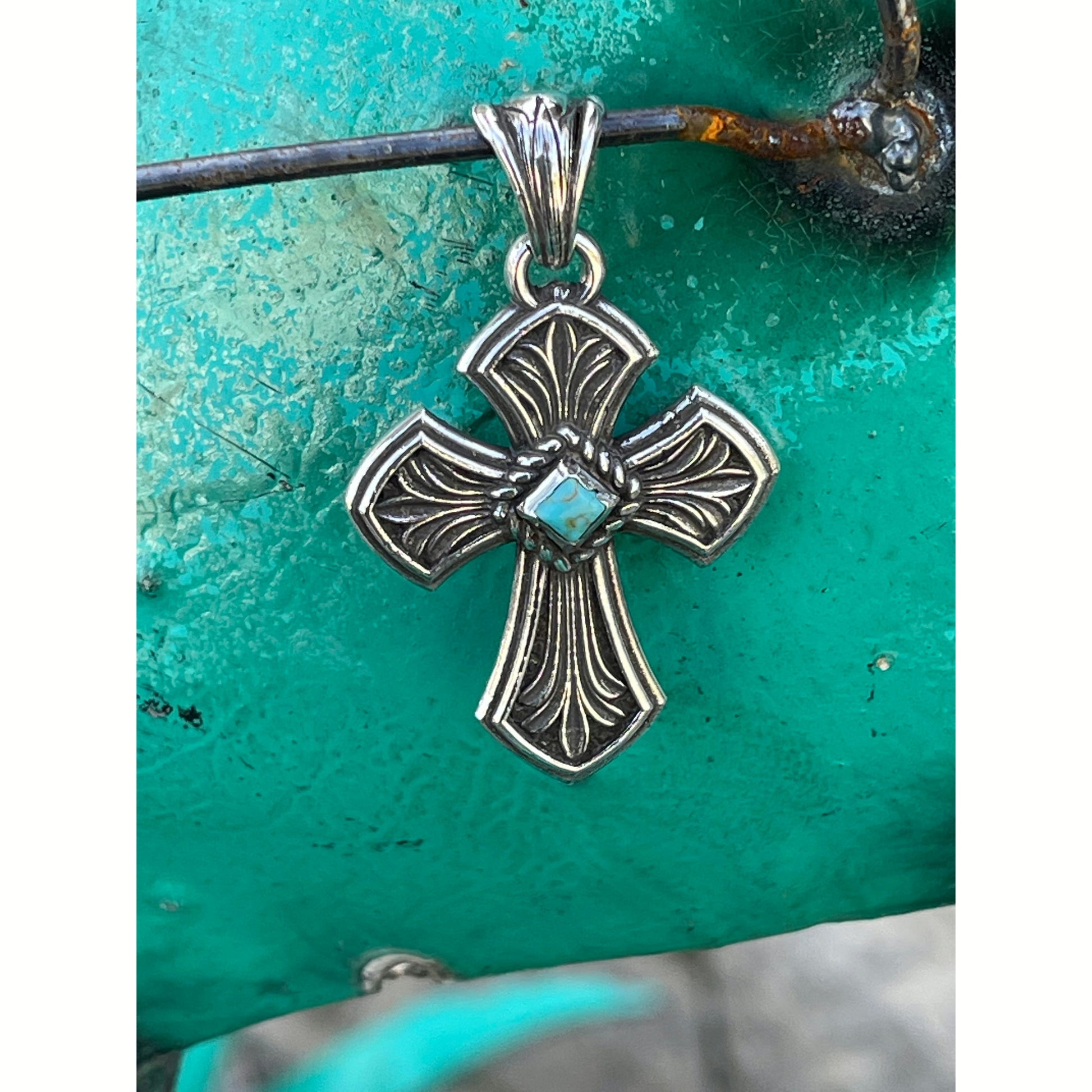 Lennon is 2”x 1” handcrafted sterling silver pendant with diamond shaped Kingman Turquoise Stone set in the middle of cross which is surrounded by a roped border.